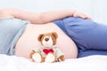 Teddy bear next to the belly of a pregnant woman.
