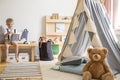 Teddy bear next to grey scandinavian tent in stylish boy`s bedroom with furniture made from natural materials, real photo with