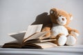 Teddy bear and opened book on grey