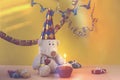 a teddy bear in a party hat against the background of garlands and gifts sits in front of muffins with a lit candle Royalty Free Stock Photo