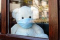 Teddy bear with protective medical mask looks out of the window on quarantine. Stay home concept Royalty Free Stock Photo