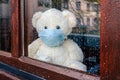 Teddy bear with protective medical mask looks out of the window with rain drops on quarantine. Stay home concept Royalty Free Stock Photo