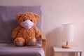 Teddy bear representative of a child wearing a face mask sits on the sofa in the living room loneliness and Sadness. Coronavirus