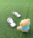 Teddy bear sitting on the grass with flip flops . Royalty Free Stock Photo