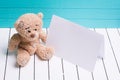 Teddy bear sitting on white wooden floor in blue-green background with blank note Royalty Free Stock Photo