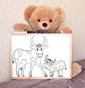 A Teddy bear toy holds a drawing Board with a cow pattern with a calf