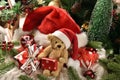 Teddy bear toy in Santa hat sitting with presents in front of Christmas tree and big red hat Royalty Free Stock Photo