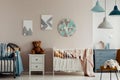 A teddy bear, two beds and a large clock on a beige wall in bright and warm bedroom interior for twins. Real photo Royalty Free Stock Photo