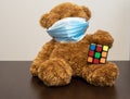 Teddy bear with virus mask plays with a colorful rubbik cube