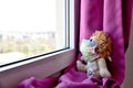 A teddy bear waering a medical protective mask sits on a windowsill and looks out the window. Sadness and loneliness during Royalty Free Stock Photo