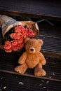 A teddy brown bear sits on wooden steps next to chrysanthemums.