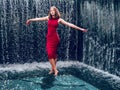 Teen ager girl in high fashion red dress posing in water, water fall behind her back. Prom photoshoot in beautiful location Young Royalty Free Stock Photo