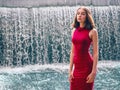 Teen ager girl in high fashion red dress posing in water, water fall behind her back. Prom photoshoot in beautiful location Young Royalty Free Stock Photo