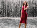 Teen ager girl in high fashion red dress posing in water, water fall behind her back. Prom photoshoot in beautiful location Young Royalty Free Stock Photo