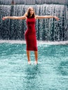 Teen ager girl in high fashion red dress posing in water, water fall behind her back. Prom photoshoot in beautiful location Young Royalty Free Stock Photo