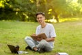 Teen Asian Guy Studying With Book Outdoors In Park And Taking Notes Royalty Free Stock Photo