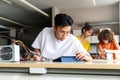 Teen asian high school student using tablet to read instructions in electronics class. Classmates in background Royalty Free Stock Photo