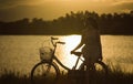 teen asian woman sit at retro vintage bicycle near the lake at sunset moment. silhouette bicycle at the sunset with grass field. Royalty Free Stock Photo