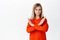 Teen blond girl showing cross, stop rejection gesture, prohibit smth, disagree, showing taboo block, standing over white