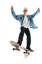 Teen boy in blue jeans shirt and cap in motion, training with skateboard, doing stunts isolated over white background Royalty Free Stock Photo