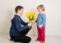 Teen boy congratulates his little sister and gives her flowers tulips