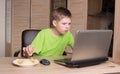 Teen boy eating potatoes chips and surfing on internet or playing video games on laptop. Kid in headphones eating chips while