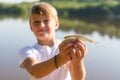 A teen boy enjoying catch. Young blond boy holding a fish outside in sunny summer day. Childhood and adventure concept.