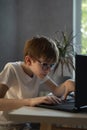 Teen boy in glasses enthusiastically plays computer games. Schoolboy does homework at computer. Homeschooling