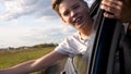 Teen boy looks out the car window and waves. The car is moving on a country road