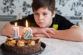 Teen boy looks thoughtfully at cake with candles on twelfth day of birth