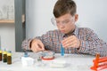 Teen boy is mixing blue liquid and powder in tube doing chemistry experiments.