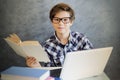 Teen boy reading book and use laptop at home Royalty Free Stock Photo