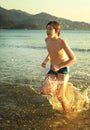 Teen boy runnung in the sea on mountain beach background smiling