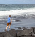 Teen boy runs along a black volcanic beach