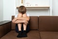 Teen boy sitting on couch with his arms around his knees. Domestic violence concept. Quarrels in family