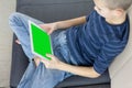 Teen boy using tablet pc with green screen while sitting on sofa at home. Close up of thumb scrolling up through touch screen