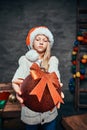 Teen boy wearing Santa`s hat holding a big Christmas ball in a dark room with a decorated wooden ladder. Royalty Free Stock Photo