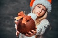 Teen boy wearing Santa`s hat holding a big Christmas ball on a dark textured background. Royalty Free Stock Photo