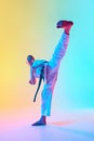 Teen boy, young martial artist demonstrating defensive techniques against gradient orange blue background in neon light