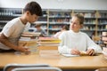 Teen brings stack of book to his girlfriend in school library Royalty Free Stock Photo