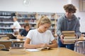 Teen brings stack of book to his girlfriend in school library Royalty Free Stock Photo