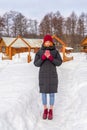 Teen cute girl in black down jacket, blue cropped jeans, burgundy hat, boots and fingerless gloves standing outdoor against winter Royalty Free Stock Photo