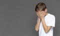 Desperate boy hiding face in palms, grey panorama background Royalty Free Stock Photo