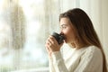 Teen drinking coffee looking through a window a rainy day