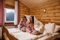 Teen friends in same Christmas pajamas relaxing in bed inside cozy log cabin with winter view Royalty Free Stock Photo