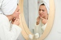 Teen girl with acne problem squeezing pimple near mirror