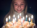 Teen girl admires burning candles at cake on her birthday. Royalty Free Stock Photo