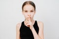 Teen girl with in a black T-shirt holds index finger in front of lips