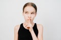 teen girl with in a black T-shirt holds index finger in front of lips.