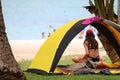 Teen girl camping and relaxing near the tent on the coconut beach